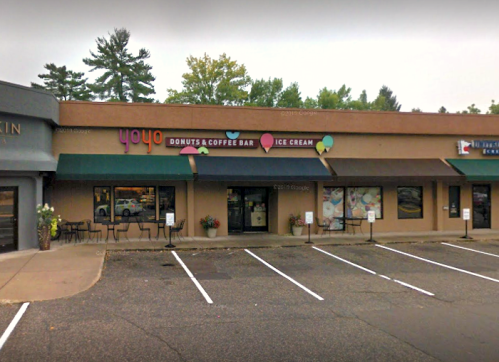Exterior of a donut and coffee shop with colorful signage, featuring outdoor seating and a parking lot.