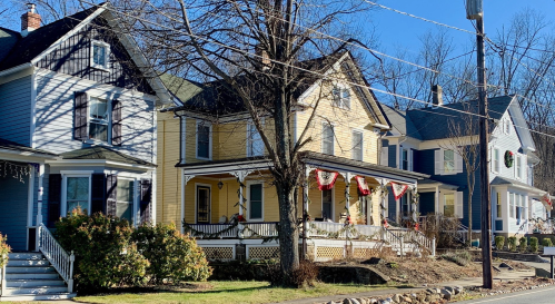 A row of colorful houses with porches, decorated for the holidays, under a clear blue sky.