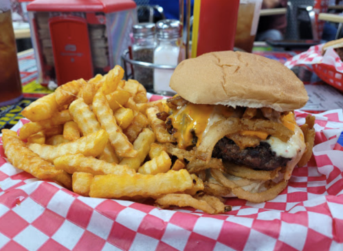 A juicy burger topped with cheese and crispy onions, served with a side of golden French fries on a checkered tablecloth.