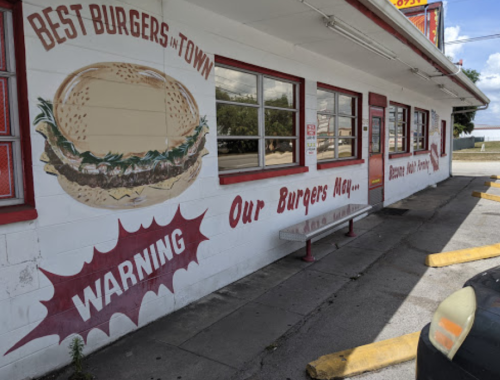 Mural on a restaurant wall advertising "Best Burgers in Town" with a warning about the burgers. Outdoor seating visible.