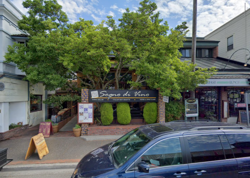 A restaurant named "Sogno di Vino" with outdoor seating, surrounded by greenery and a blue sky. A parked car is in the foreground.