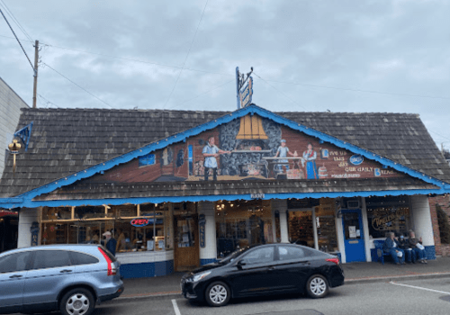 A colorful mural on a shopfront depicts people working, with a blue roof and "OPEN" sign visible. Cars parked outside.