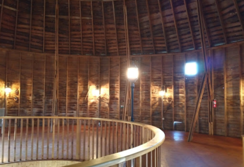 Interior of a circular wooden room with a high ceiling, featuring wooden beams and soft lighting.