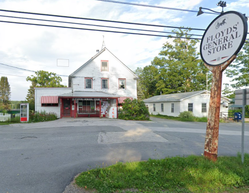 A quaint general store with a red and white striped awning, surrounded by greenery and a sign reading "Floyd's General Store."