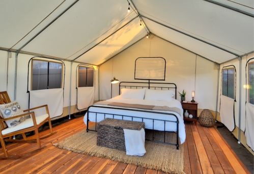 Cozy glamping tent interior featuring a bed, wooden flooring, and stylish decor.
