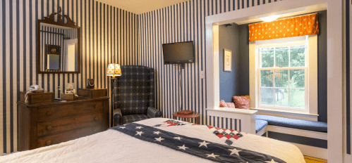Cozy bedroom with striped walls, a quilted bed, a TV, and a window seat with a view.
