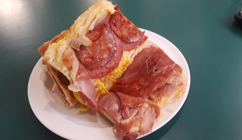 A plate with two stacked sandwiches filled with various meats and cheese on a green table.