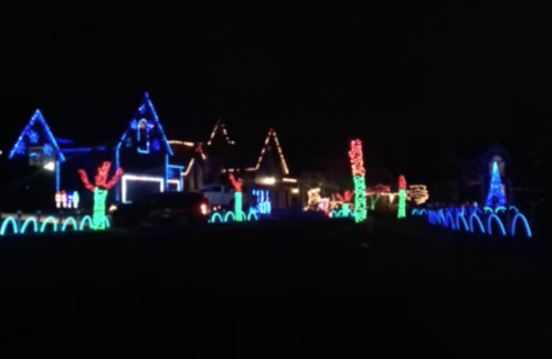 Colorful holiday lights decorate several houses and trees in a festive nighttime display.