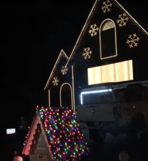 A brightly lit house decorated with snowflake lights and a colorful, illuminated gingerbread house in the foreground.