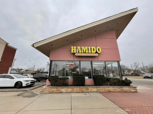 Exterior of Hamido Restaurant, featuring a modern design with large windows and a distinctive angled roof.