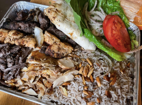 A metal tray filled with rice, grilled meats, lettuce, tomato, and onions, garnished with herbs.
