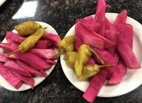 Two white plates with vibrant pink radish slices and yellow peppers, arranged neatly on a dark countertop.