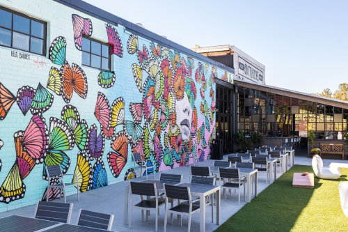 Colorful butterfly mural on a brick wall beside an outdoor seating area with tables and chairs.