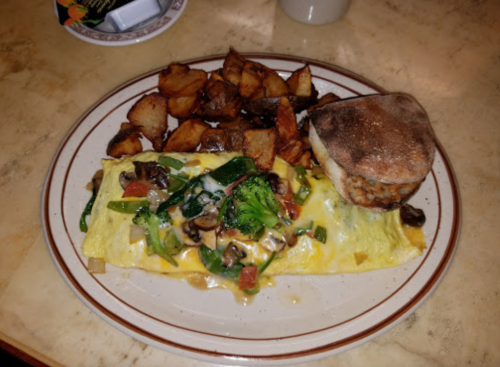 A plate with a vegetable omelette, topped with cheese, and a side of golden-brown potato wedges.