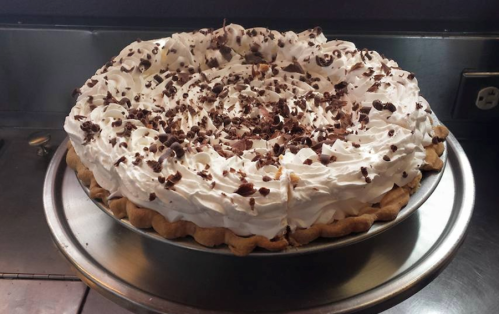 A delicious chocolate cream pie topped with whipped cream and chocolate shavings, sitting on a silver pie plate.