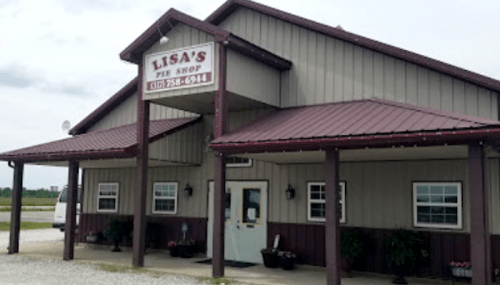 A rustic pie shop with a sign reading "Lisa's Pie Shop," featuring a metal roof and gravel parking area.