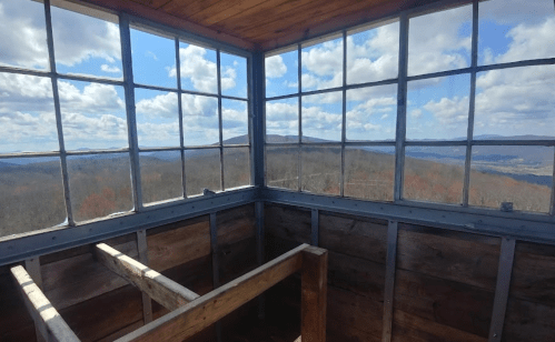 View from inside a lookout tower, featuring large windows and a scenic landscape of hills and clouds outside.
