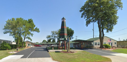 A colorful tower stands in front of a single-story building surrounded by trees and a clear blue sky.