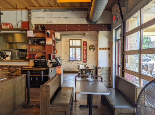 Interior of a casual dining space with wooden benches, a table, and a large open window. Bright and inviting atmosphere.