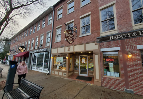 A brick storefront with a sign reading "Harvey's" and an open door, alongside other shops on a rainy day.