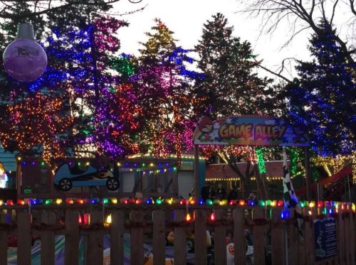 Colorful lights adorn trees and a sign for "Game Alley" in a festive outdoor setting.