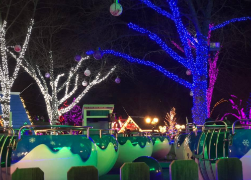 Colorful illuminated trees and festive decorations surround a whimsical ride at night, creating a magical atmosphere.