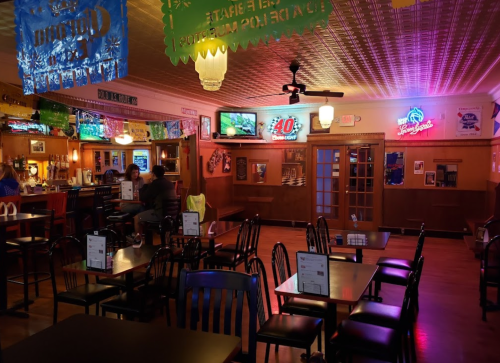 A cozy bar interior with empty tables, neon lights, and a TV, creating a relaxed atmosphere.