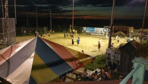 A vibrant sunset over a sand volleyball court, with players and spectators enjoying the evening atmosphere.