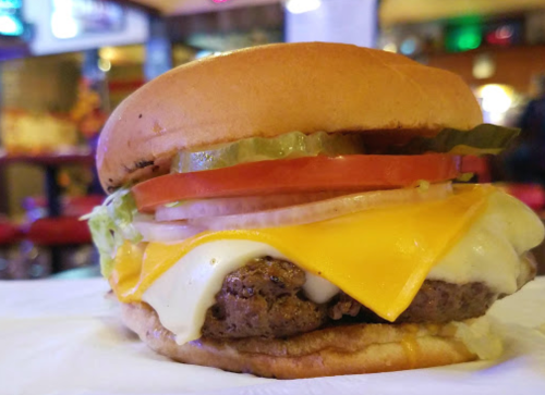 A close-up of a cheeseburger with lettuce, tomato, pickles, and melted cheese on a toasted bun.