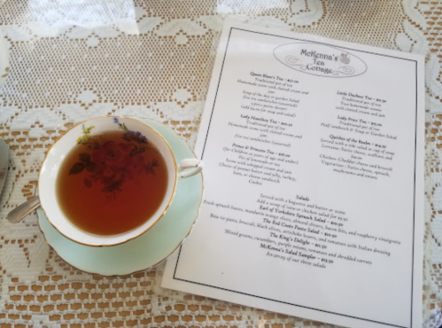 A cup of tea on a lace tablecloth next to a menu for McKenna's Tea Cottage.