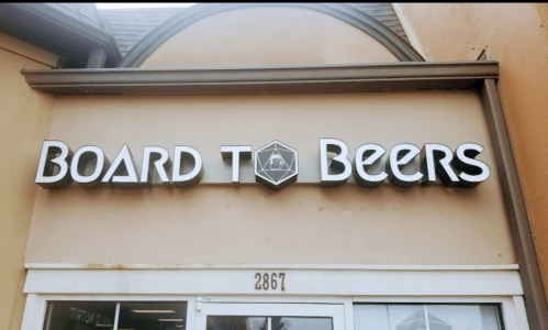 Sign for "Board to Beers" storefront, featuring bold lettering against a light-colored building.