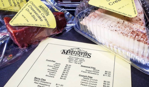A menu and dessert items, including cheesecake and pies, displayed with price tags on a table.