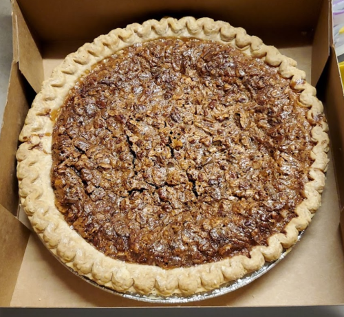 A freshly baked pecan pie in a cardboard box, featuring a golden crust and a rich, nutty filling.