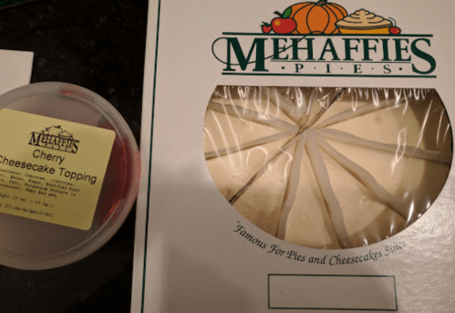 A box of cheesecake slices next to a container of cherry topping, both from Mehaffies Pies.