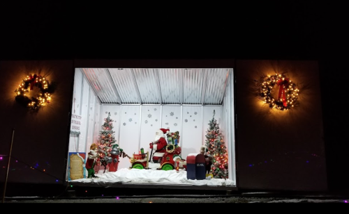 A festive display featuring Santa on a toy truck, surrounded by Christmas trees and decorations in a snowy setting.