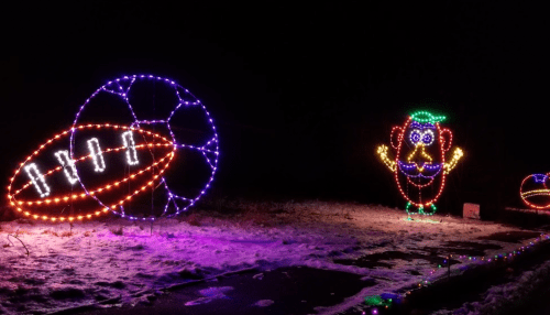 Colorful holiday lights display featuring a football, soccer ball, and a whimsical character in a winter setting.