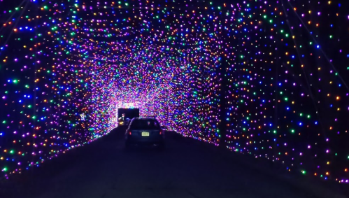 A car drives through a colorful tunnel of bright, twinkling lights in various colors.