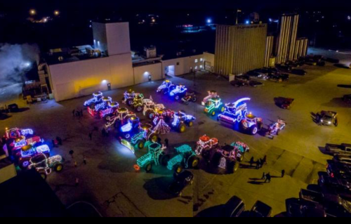 Aerial view of brightly lit tractors decorated with colorful lights, gathered in a parking lot at night.