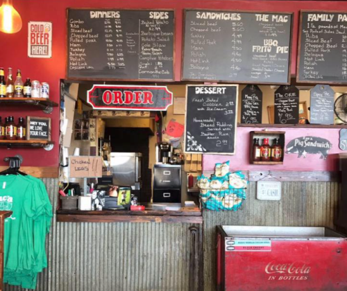 A rustic restaurant counter with a menu board, drinks, and a vintage Coca-Cola cooler. Cozy and inviting atmosphere.