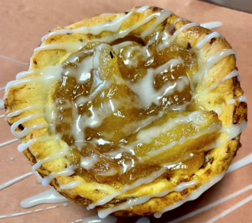 A close-up of a cinnamon roll topped with apple filling and drizzled with icing on a brown paper background.