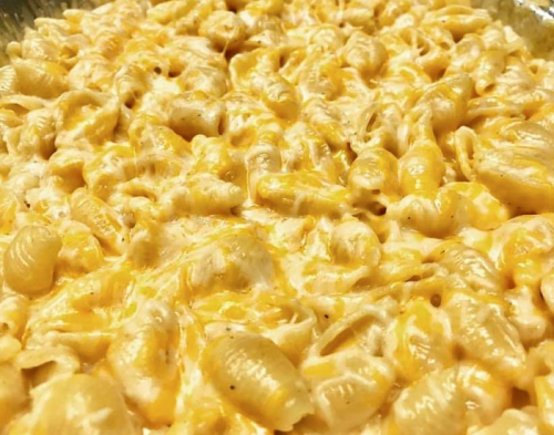 Close-up of creamy macaroni and cheese with a golden, cheesy topping, featuring shell-shaped pasta.