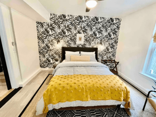 Cozy bedroom featuring a black and white leaf-patterned wall, a bed with yellow throw, and stylish decor.