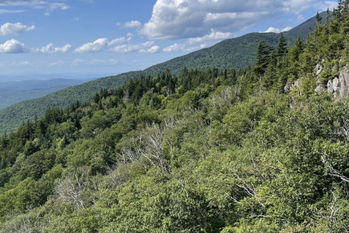 Lush green mountains under a blue sky with scattered clouds, showcasing a vibrant natural landscape.