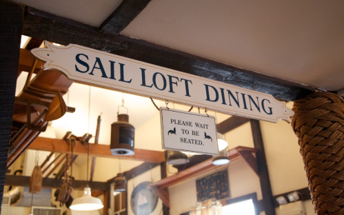 Sign for "Sail Loft Dining" with a "Please wait to be seated" notice, set in a cozy, rustic dining area.