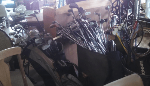 A collection of golf clubs and a golf bag, surrounded by various sports equipment in a cluttered space.