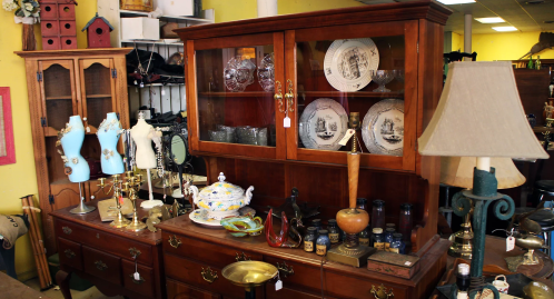 A vintage display featuring a wooden cabinet, decorative plates, lamps, and various antique items on a table.