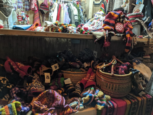 A colorful display of knitted hats, gloves, and sweaters in a cozy shop, with baskets overflowing with handmade items.