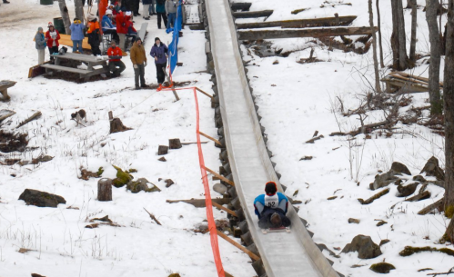 A snowy landscape with a sledding ramp and people enjoying winter activities in the background.