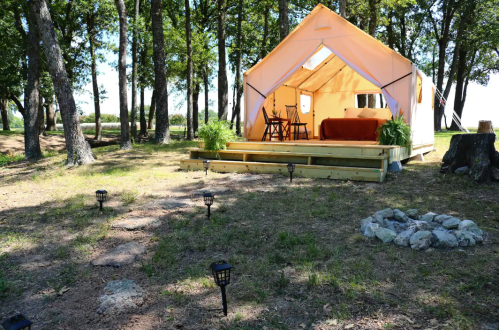 A cozy tent on a wooden platform surrounded by trees, with a small table and chairs outside.