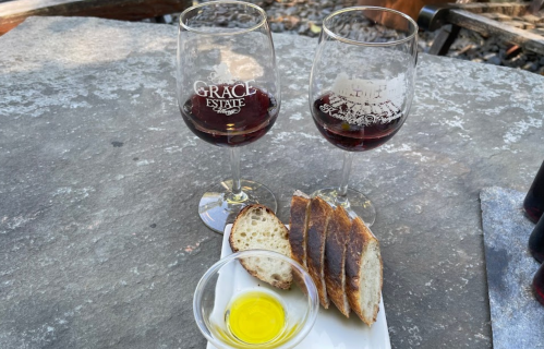 Two glasses of red wine beside a plate of sliced bread and a small dish of olive oil on a stone table.